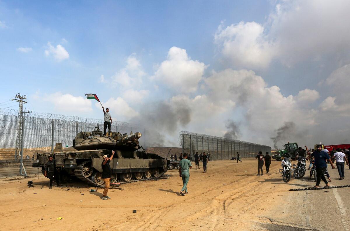 الفلسطينيون يلوحون بعلمهم الوطني ويحتفلون أمام دبابة إسرائيلية مدمرة في قطاع غزة.  الصورة: ا ف ب