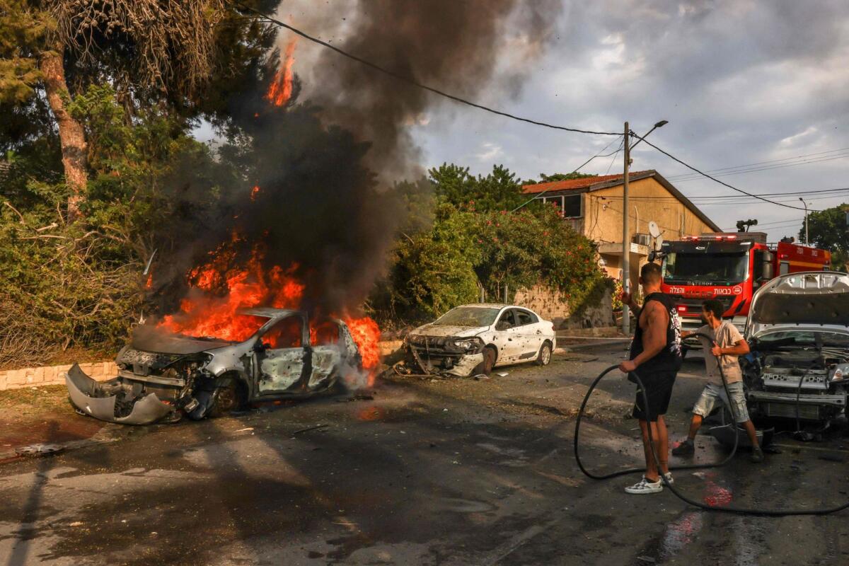 أشخاص يخمدون حريق سيارة في مدينة عسقلان بجنوب إسرائيل بعد هجوم صاروخي من غزة، 9 أكتوبر، 2023. — AFP