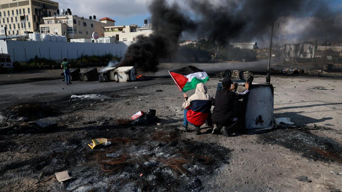 فلسطينيون يختبئون خلف حاوية خلال اشتباكات مع القوات الإسرائيلية بالقرب من رام الله بالضفة الغربية في 18 أكتوبر. — رويترز