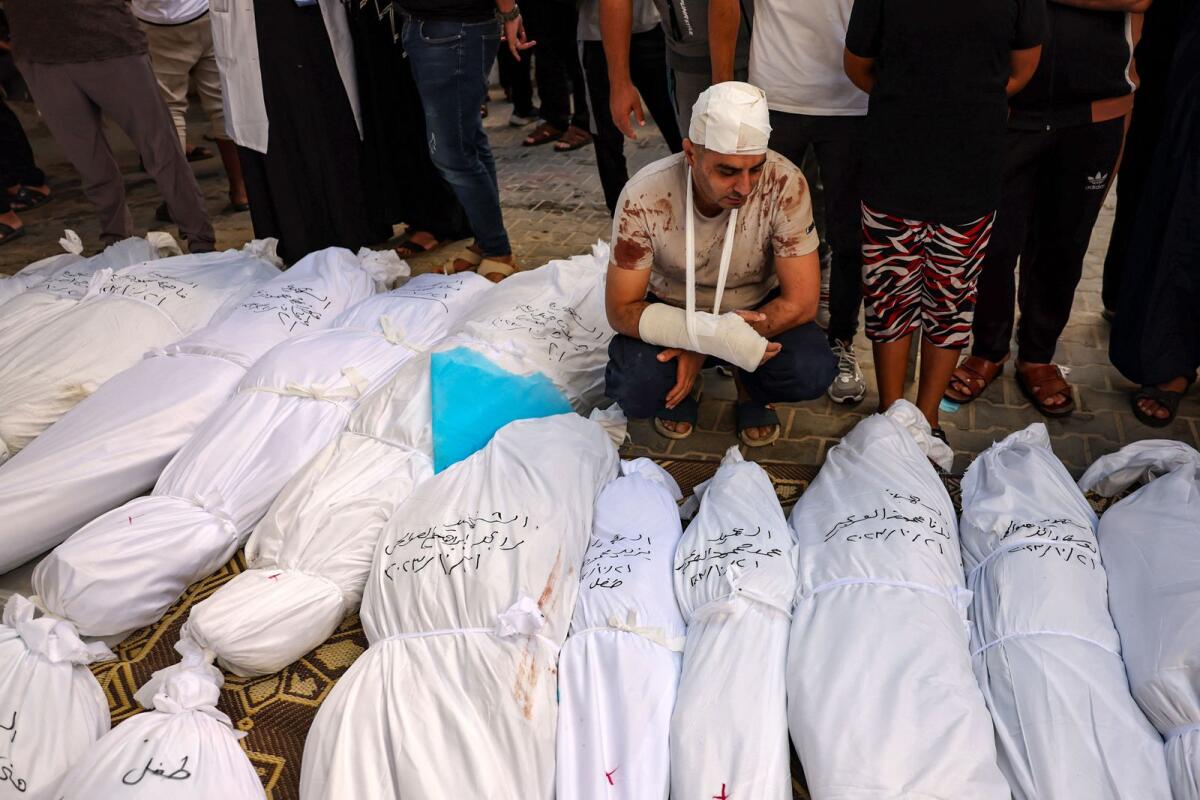 الفلسطيني المصاب محمود العرير يقف بالقرب من جثث أطفاله الملقاة بين الجثث الأخرى، الذين قتلوا في قصف إسرائيلي على رفح بجنوب قطاع غزة في 21 أكتوبر 2023. AFP