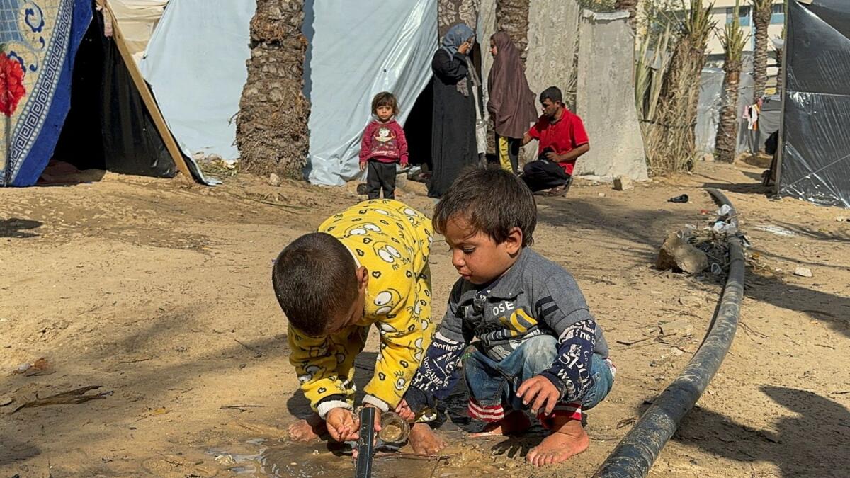 أطفال فلسطينيون يحصلون على المياه من أنبوب، بينما لجأ الفلسطينيون النازحون الذين فروا من منازلهم بسبب الغارات الإسرائيلية إلى مخيم في خان يونس.  – رويترز