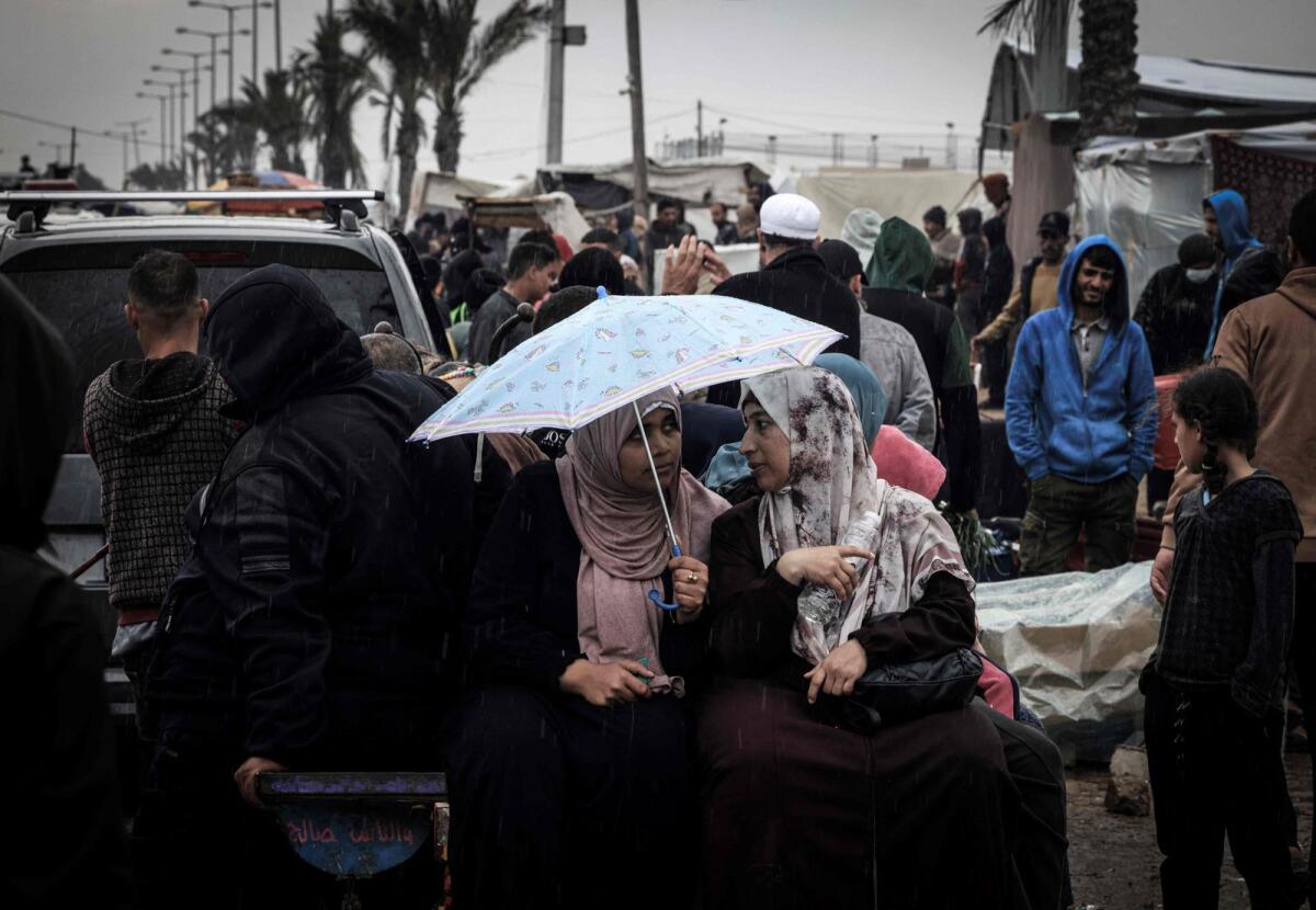 نساء فلسطينيات يتحدثن تحت مظلة في مخيم مؤقت يؤوي الفلسطينيين النازحين في رفح جنوب قطاع غزة.  – وكالة فرانس برس