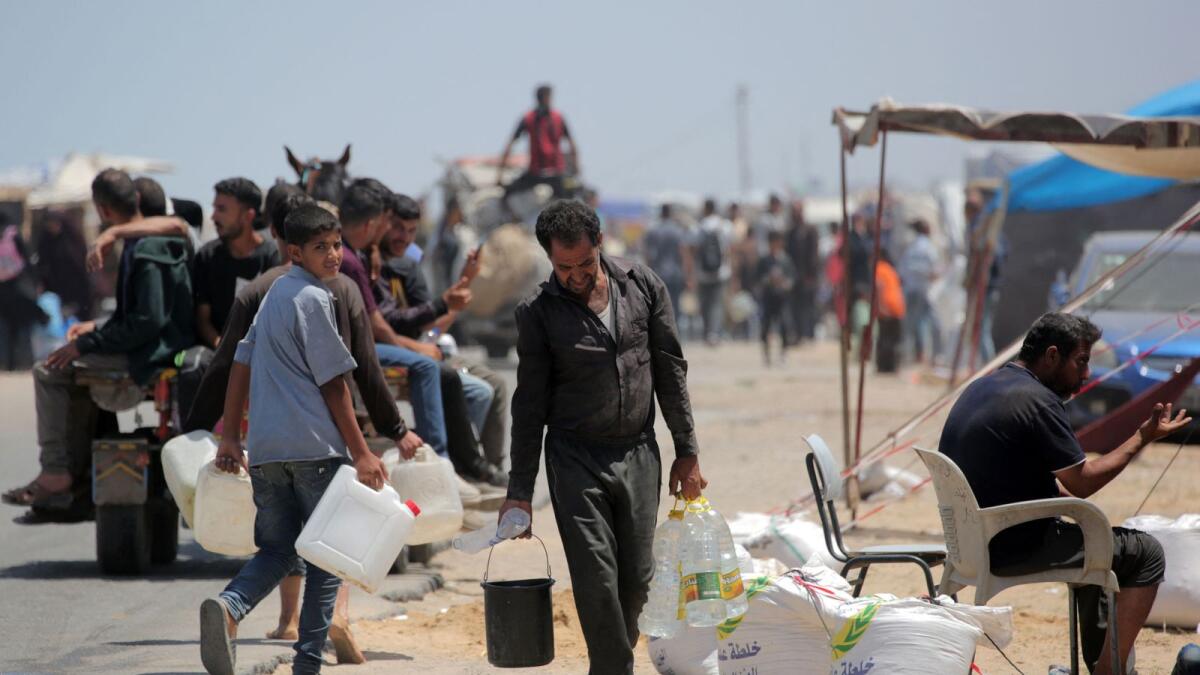 فلسطينيون لجأوا إلى دير البلح بعد فرارهم من رفح في جنوب قطاع غزة، يحملون المياه إلى خيامهم في مخيم مؤقت.  – الصورة: وكالة فرانس برس