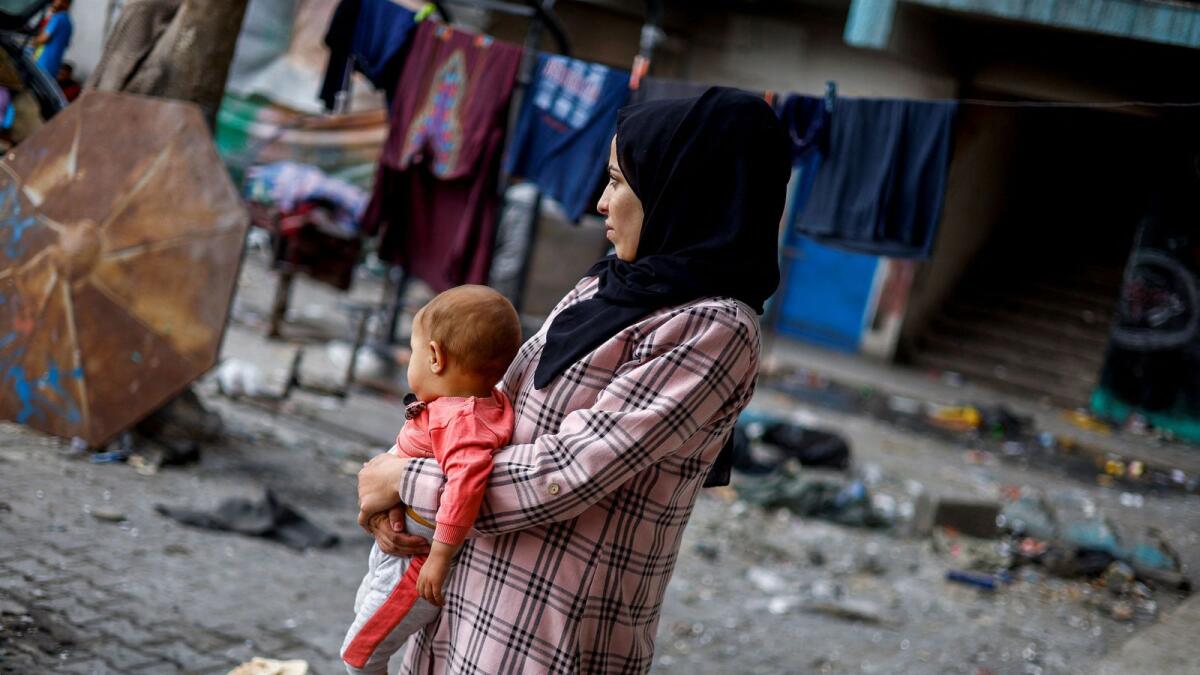 امرأة فلسطينية تحمل طفلها في مدرسة شبه مهجورة تستخدم كملجأ للنازحين الذين فروا من رفح بعد أن شنت القوات الإسرائيلية عملية برية وجوية.  – الصورة: رويترز